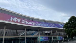 A large banner reading HPE Discover Barcelona 2024 on the side of the Fira de Barcelona. The words sit atop a red and purple image containing strands of energy and sparks. 