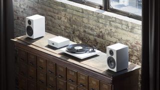 A white Pro-Ject Essential III turntable on a cabinet, flanked by two white desktop speakers