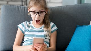 Child girl looking at mobile phone at home, with a surprised expression on her face