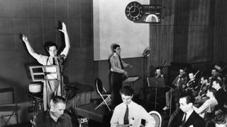 men in suits speak into microphones on a soundstage