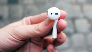 En hand håller upp en Apple AirPods mot en suddig bakgrund.