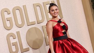 Selena Gomez wears a red dress and poses for photos on the red carpet in front of a sign reading Golden Globes