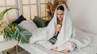 A woman sits up in bed drinking a bedtime time to help her sleep better