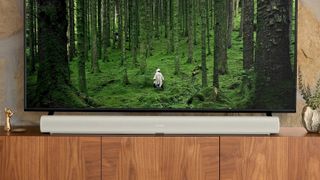 Sonos Arc standing on a wooden unit beneath a TV screen