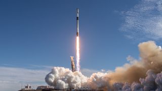 a black-and-white spacex falcon 9 rocket launches into a blue sky.