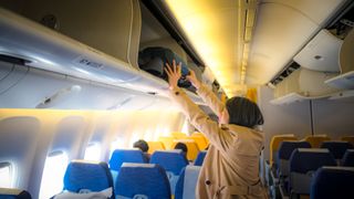 Traveler placing her bag in the overhead storage compartment of a plane