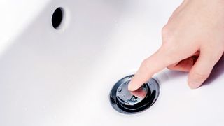 Finger pushing down chrome pop up sink plug