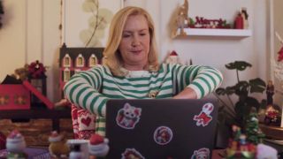 Angela Kinsey typing up a Christmas letter in Confessions of a Christmas Letter on Hallmark. 