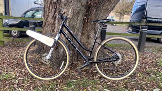 a black city bike is photographed with the CLIP e-bike conversion kit attached to the front wheel