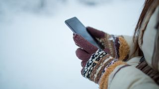 Female hands holding a cellphone outdoors in the snow