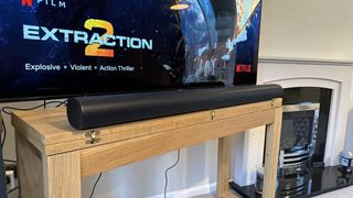 A black Sonos Arc in front of a TV on top of a wooden table in a living room