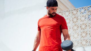 Man holding two dumbbells looking down at the weight, outdoors