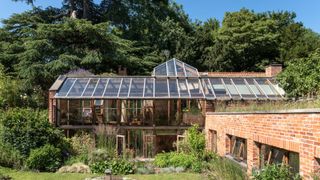 A conservatory in a garden that also has a bricked wall running across the garden