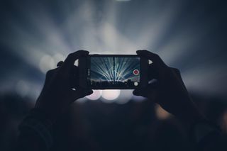 Hands holding up phone camera to video a gig