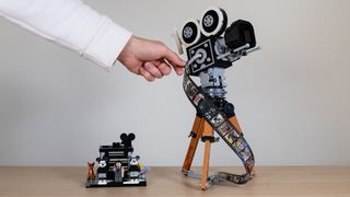 The Lego Disney Walt Disney Tribute Camera. A hand operates the hand crank on the 1920s film camera, with the multi-plane camera side build next to it 