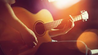 Young guitarist in a black t-shirt bathed in orange light and holding an acoustic guitar