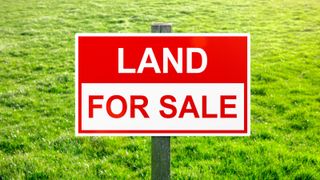 Land for sale sign in green grass field for housing development and construction background