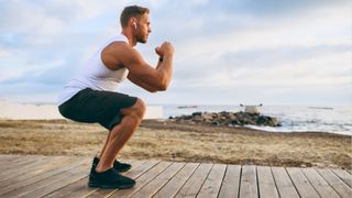 Man performing bodyweight squat outside by the ocean during outdoor workout