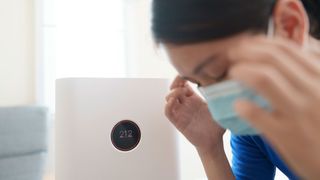 A woman in a face mask standing next to an air purifier