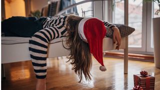 A woman lying on her front in bed fast asleep wearing a christmas hat