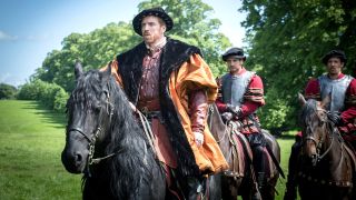 Damian Lewis as Henry VIII sits atop a horse, flanked by soldiers, in the English countryside in Wolf Hall: The Mirror and the Light