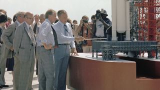 as press photographer take photos, nasa officials briefs the president of the united states about the space shuttle beside a larger outdoor model of the winged vehicle.