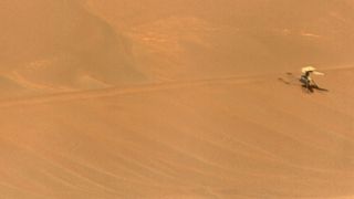 a small dual-rotor helicopter lays dormant on a reddish-orange sand dune