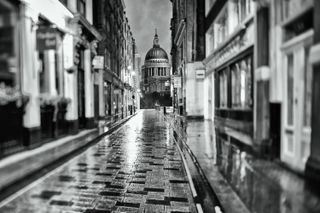 St Pauls Cathedral in London seen through narrow street in black and white, high contrast, rain reflections