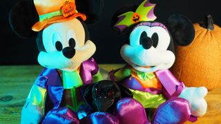 Mickey, Minnie, and Raven plush toys on a wooden table in front of a pumpkin