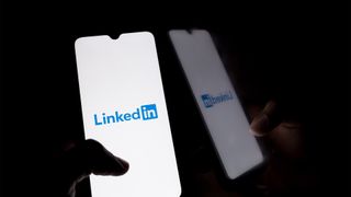 LinkedIn logo and branding pictured on a smartphone screen held by shadowed handed.