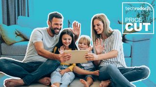 Family of four sitting around a tablet looking happy and waving. The TechRadar logo and &quot;Price Cut&quot; is in the top right in white. The background is light blue.