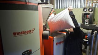 A man pours a bag of wood pellets into a biomass boiler