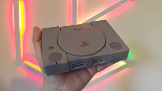 Hand holding PS1 Mini console with red and green lights in backdrop