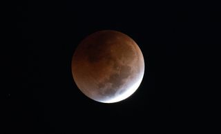 photo of a lunar eclipse, showing most of the moon obscured in reddish-brown shadow