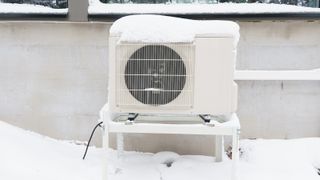 A heat pump unit outside in the snow against a light wall