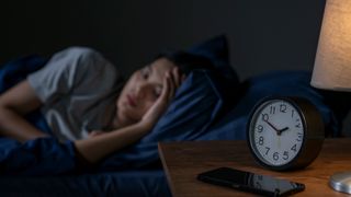 Woman sleeping next to a clock to indicate a consistent bedtime