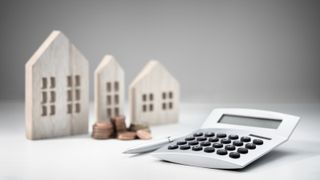 Calculator and pen, piles of coins, and three small models of houses