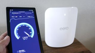 A phone running a speed test next to the eero Max 7 mesh router