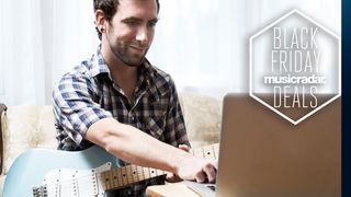 Man holding a blue electric guitar types on a laptop