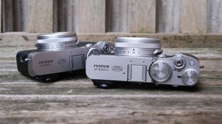 Fujifilm X100VI camera next to a Fujifilm X100V camera on a slatted wooden bench