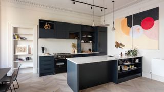 contemporary navy kitchen with island, banks of rear wall unites, white bookshelf to side and vibrant modern art on wall