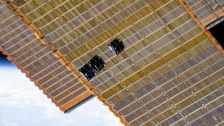 A photo of very small, black cube-shaped satellites in space with the ISS in the background