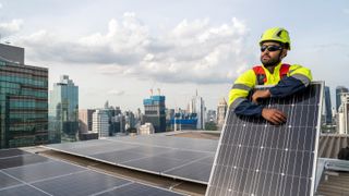 A solar panel installer on a roof holding a solar panel