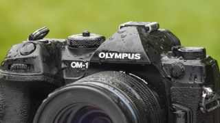 OM System OM-1 mirrorless camera outdoors, coated in rain water and bright green grass background