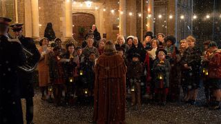 A brass band accompanies a cosy choral performance as it snows in the glowing, golden light outside in the Call the Midwife Christmas Specials 2024.