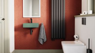 A bold and modern small bathroom with textured terracotta walls, a chic green wall-mounted sink, and a sleek black radiator.