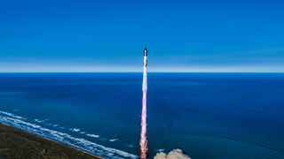 a giant silver rocket launches into a blue sky, with the ocean in the background