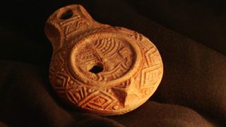 A close-up of a molded clay oil lamp. It has a menorah decoration on its top.