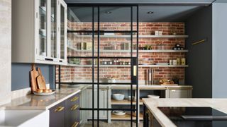 walk in pantry area with exposed brick wall and open shelving behind sliding black framed glass doors 