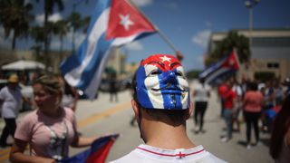 A guy with a mask of Guy Fawkes painted with the Cuban flag colour during a protest